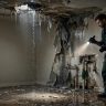 Inspector checking a leaky room with wet walls, exposed pipes, and standing water.