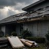 A suburban home with damaged shingles and roofing documents beside replacement materials.